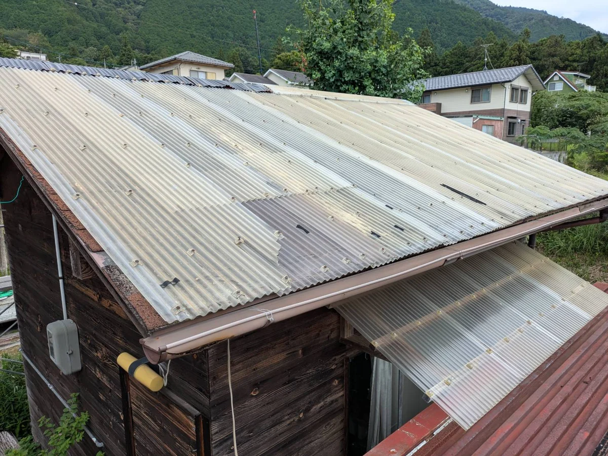 葺き直し前の納屋の屋根。古いポリカ波板が色あせ、繰り返し補修された跡がある状態